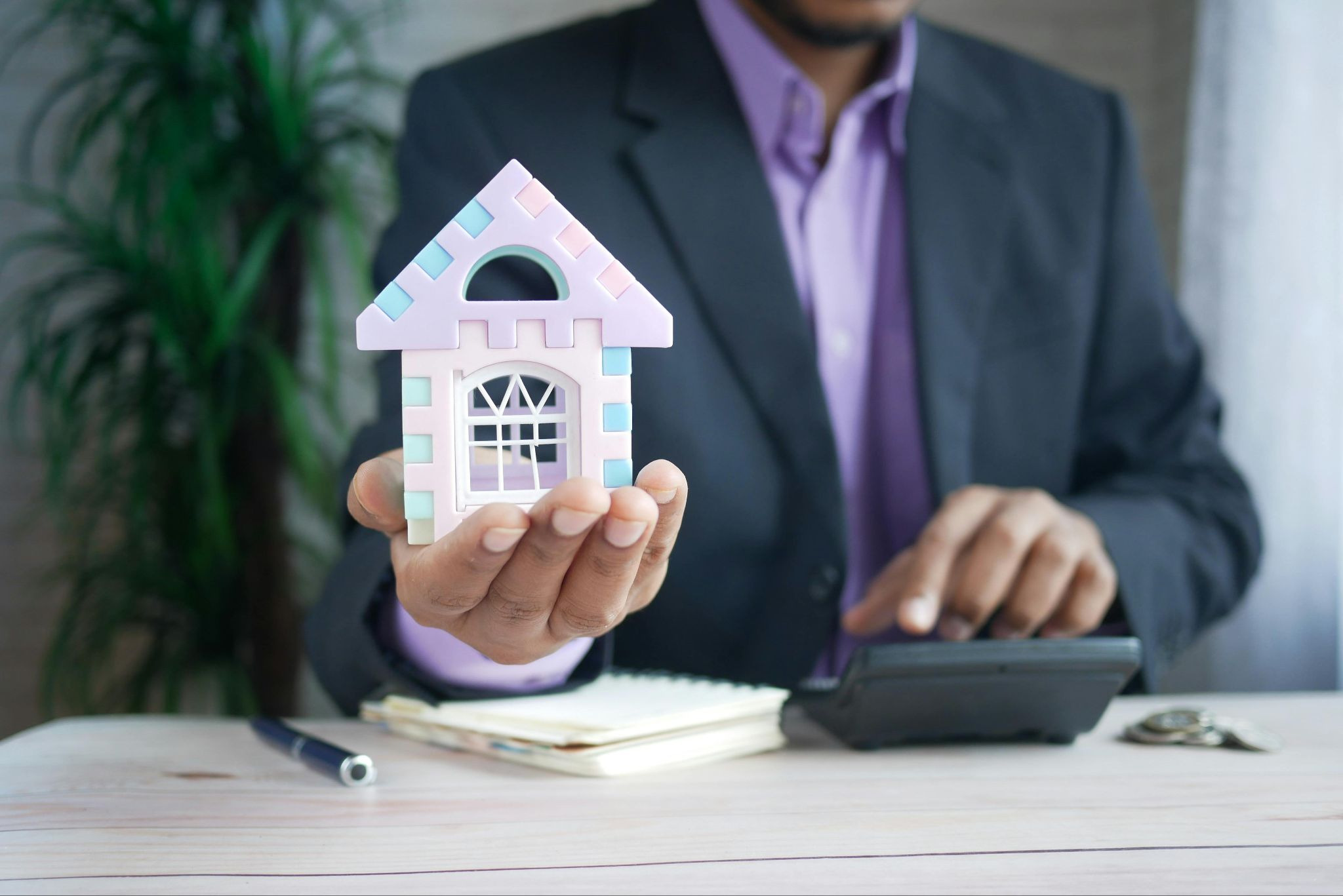 Property Manager holding a foam model house with their right hand and using a calculator with their left hand.